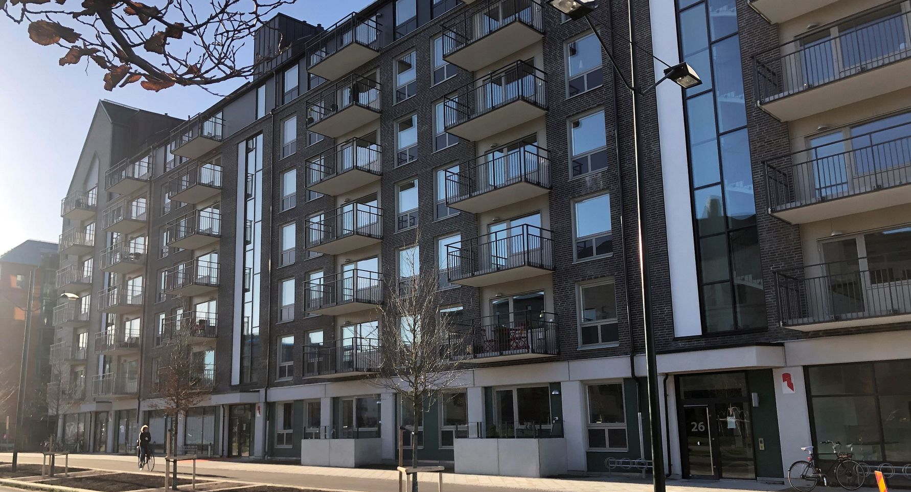 Modernt lägenhetskomplex i flera våningar med balkonger, stora fönster och en gångväg framför byggnaden