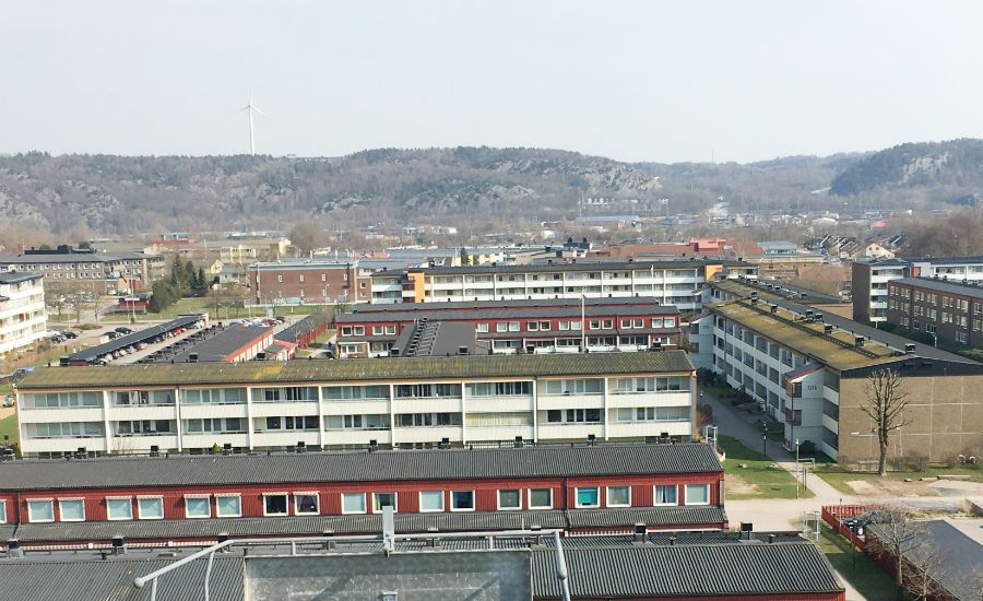 Utsikt över ett bostadsområde med flerfamiljshus, omgiven av kullar och skog i bakgrunden
