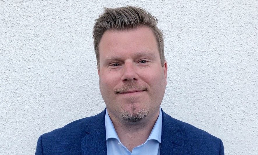 Man i blå kavaj och ljusblå skjorta framför en vägg med vit puts