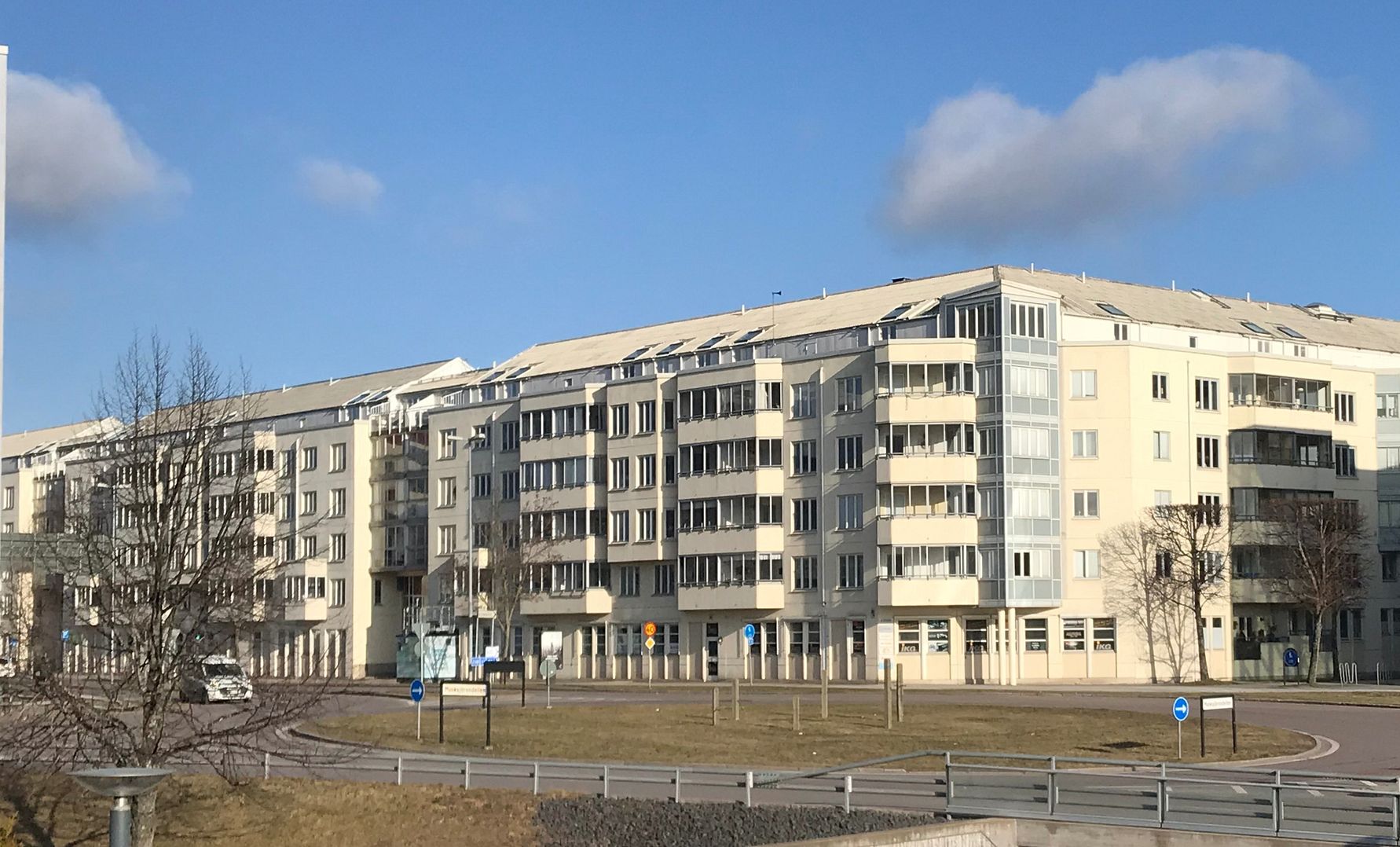 Flerbostadshus i modern stil med ljusa fasader, tomt träd och blå himmel i bakgrunden