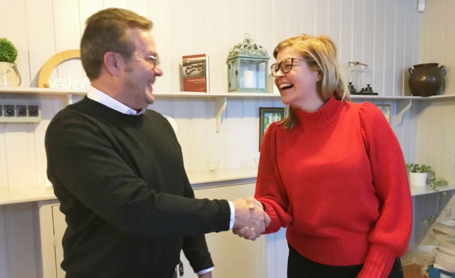 Två personer som skakar hand i ett inomhusrum med hyllor och dekorationer i bakgrunden