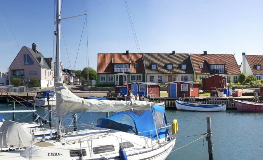 Segelbåtar förtöjda vid en hamn med färgglada hus i bakgrunden och klart blå himmel