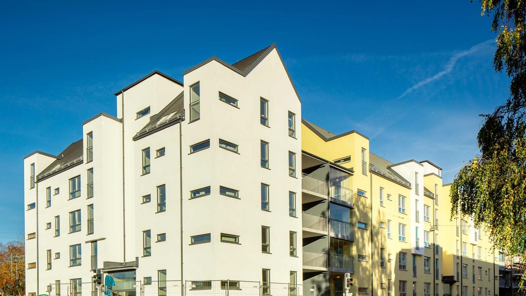 Flerfamiljshus med vita fasader och gul detalj, moderna vinklade tak och flera fönster, fotograferat under klarblå himmel