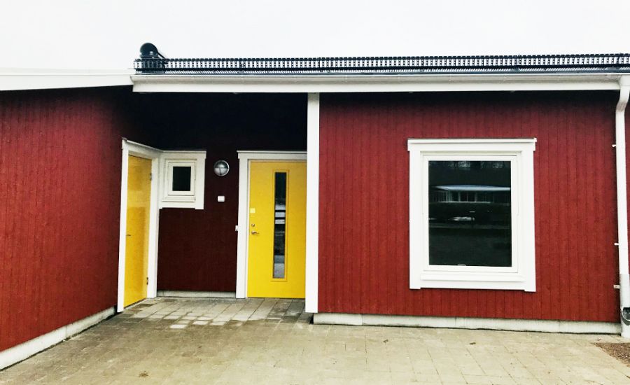 Röd byggnad med gult dörrpar, vitmålade fönster och grå stenlagt entréområde