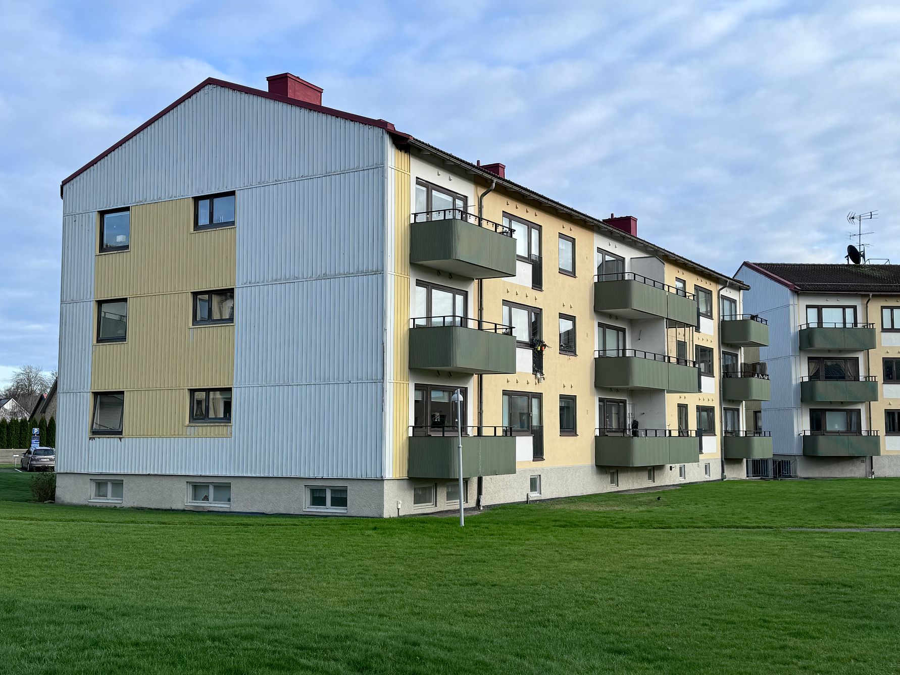 Bostadshus med flera våningar, gul och grå fasad, balkonger och grön gräsmatta framför