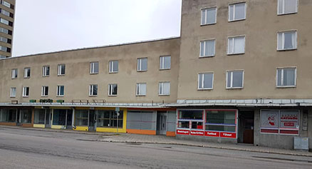 En rad med äldre hyreshus och butiker längs en tom gata, med flagnande fasader och några stängda skyltfönster
