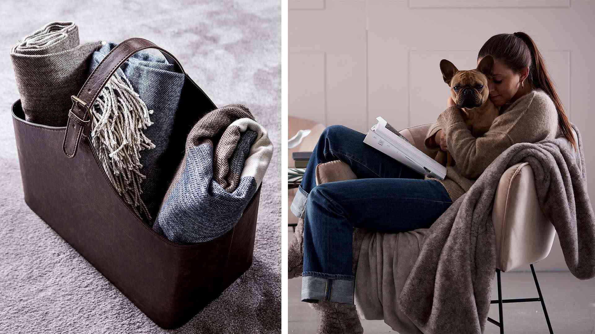 En läderkorg fylld med hoprullade plädar bredvid en kvinna som sitter i en stol, håller i en hund och läser en bok