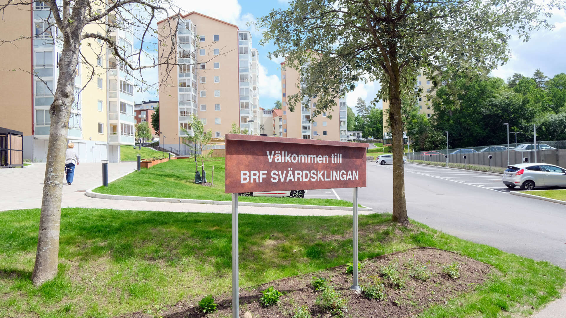 Bostadsområdet BRF Svärdsklingan med skylt i förgrunden, flervåningshus och parkeringsplats i bakgrunden