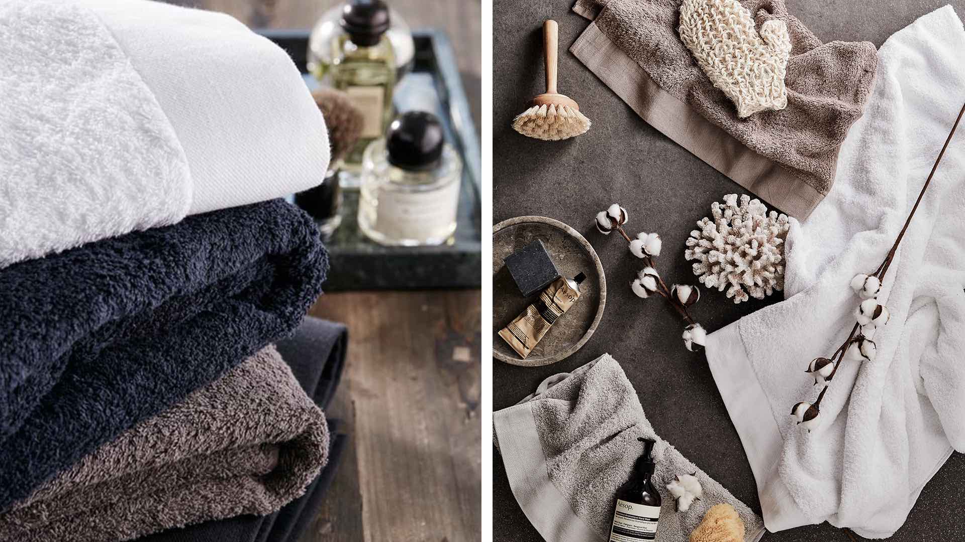Hög med hopvikta handdukar i olika färger och badrumsartiklar som borstar och oljor arrangerade på en träyta