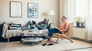 En man ligger i soffan med Ipad och en kvinna sitter i en stol med en bok. 