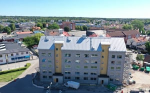 Nybyggnad av ett flerfamiljshus med grå fasad och gula detaljer, omgiven av grönska och andra byggnader i stadsmiljö