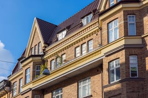 Brun tegelbyggnad med branta tak, vita fönster och en balkong under en klarblå himmel