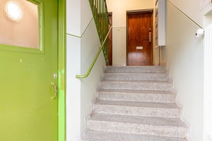 Trapphus med stentrappor och grön dörr, väggar med ljus färg och en trär dörr längst upp
