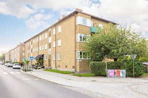 Flerfamiljshus i tegel med trottoar, parkeringsplats och övergångsställe i förgrunden