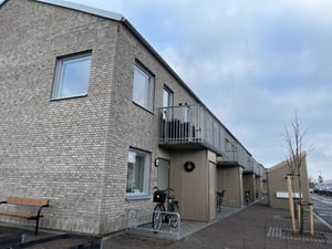 Låga byggnader med fasader av grått tegel, balkonger och cyklar parkerade framför. Vintertid med molnig himmel och torra markytor