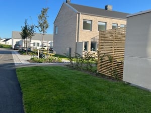 Modern bostadsområde med gräsmatta, träd, och tvåvåningshus i tegel mot en klar blå himmel