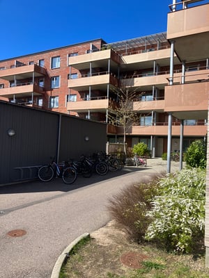 Flerfamiljshus med tegel- och putsfasad, cykelställ och grönska i förgrunden under en klarblå himmel