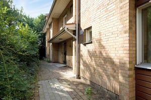 Tvåvåningshus i tegel med en gång av stenplattor, omgiven av grönska och träd