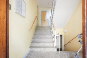 Trapphus i en bostadsbyggnad med grå trappa, ljusgula väggar och ledstänger av trä