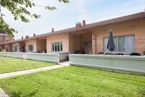 Radhus i en rad med tegelväggar, små trädgårdar och gröna gräsmattor framför en gångväg