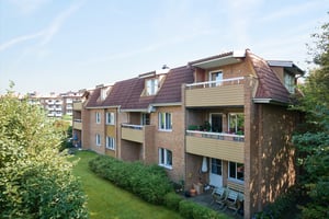 Lägenhetsbyggnad i tegel med balkonger och trädgårdsområde med gräsmatta och buskar