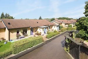 Radhus med tegelfasad och röda tak, omgivna av grönska och en asfalterad gångväg