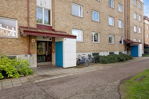 Flerbostadshus med fasad av gulbrun tegel, entré med blå dörrar och cyklar parkerade vid sidan