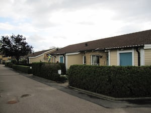 Radhus med gul fasad och bruna takpannor, omgivna av häckar, svensk flagga synlig vid en av byggnaderna, molnig himmel ovanför