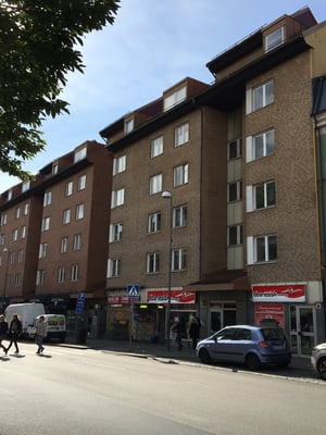 Flerbostadshus med fasad av tegel, butikslokaler på bottenvåningen och parkerade bilar längs gatan