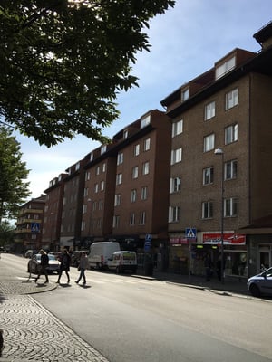 Gata med flervåningshus, butiker och människor som går över ett övergångsställe i dagsljus