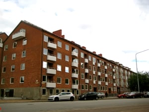 Flerbostadshus i rött tegel med flera våningar, balkonger och parkerade bilar längs gatan