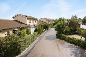 Rad av villor med trädgårdar längs en asfalterad väg under en klarblå himmel