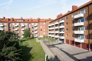 Flerfamiljshus i rött tegel med balkonger och en grön innergård under en klar himmel