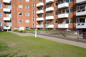 Flerfamiljshus i rött tegel med vita balkonger och en gräsmatta framför