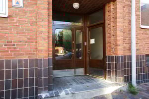 Ingång till byggnad med röda tegelväggar, mörka trädörrar och glasfönster
