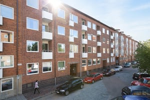 Flerbostadshus i tegel med balkonger och parkerade bilar längs gatan under en solig himmel