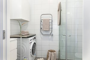 Badrum med vitkaklade väggar, tvättmaskin, handdukshängare, duschkabin och dekorativa handdukar