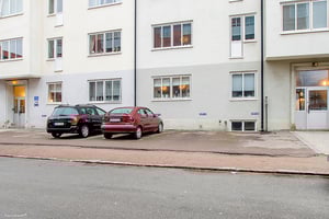 Parkering framför en vit byggnad med flera fönster, där två bilar står parkerade på asfalt
