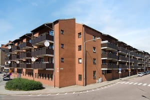 Lägenhetskomplex i tegel med flera balkonger och satellitantenner, beläget vid en gatukorsning