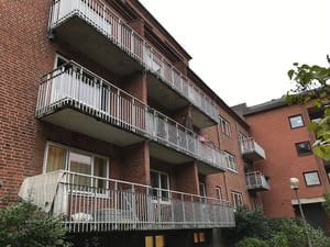 Flerfamiljshus i rött tegel med flera balkonger, omgivna av grönska