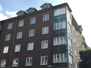 Flerbostadshus i tegel med gröna detaljer och stora fönster, under en klar himmel