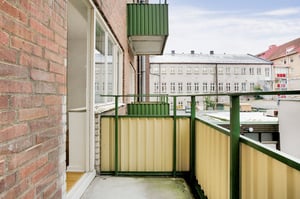 Balkong med gröna räcken och gul panel, anslutande till en tegelbyggnad, med utsikt mot en innergård och omgivande byggnader