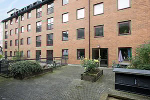 Flerfamiljshus i tegel med fyra våningar, innergård med växtlådor, staket och stenlagd yta