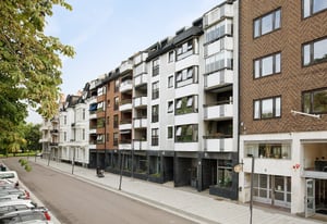 Flerfamiljshus längs en gata med parkering, träd och trottoar under en klar himmel