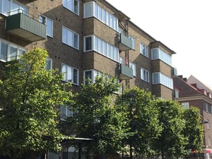 Flerfamiljshus i tegel med balkonger, stora fönster och grönskande träd framför