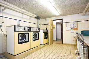 Tvättstuga med två tvättmaskiner, vägg med informationsblad och bord för vikning av kläder