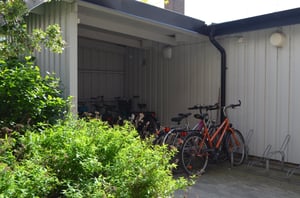 Cykelskjul vid en byggnad med flera parkerade cyklar, omgiven av grönska