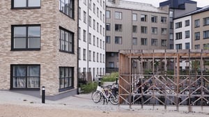 Flera moderna flerbostadshus med fasader av tegel och puts, en cykelparkering med tak i förgrunden