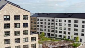 Flerfamiljshus med modern arkitektur, ljus fasad och svart tak, omgivna av en grön gård med träd och pergola