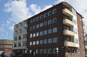 Flerbostadshus i tegel med balkonger, blå himmel och några människor synliga på marken